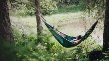 Bir kadın yürüyüşçü, dağ gölüne bakan bir hamakta dinleniyor.