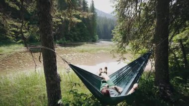 Bir kadın yürüyüşçü, dağ gölüne bakan bir hamakta dinleniyor.