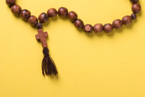 Wooden rosary and cross on yellow background.