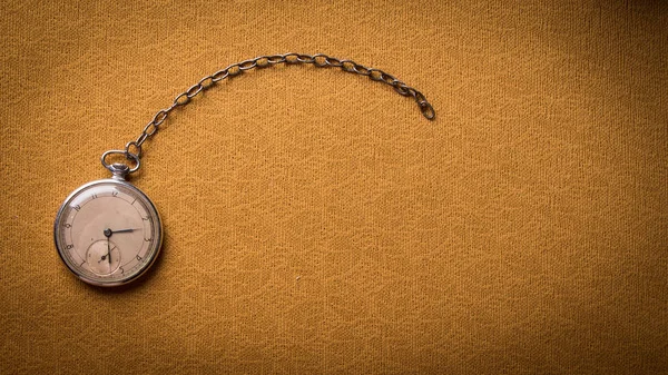 Old pocket watch on the background of a gold drapery fabric table.
