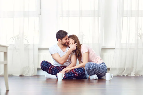 Um casal amoroso abraçando no chão contra a janela . — Fotografia de Stock