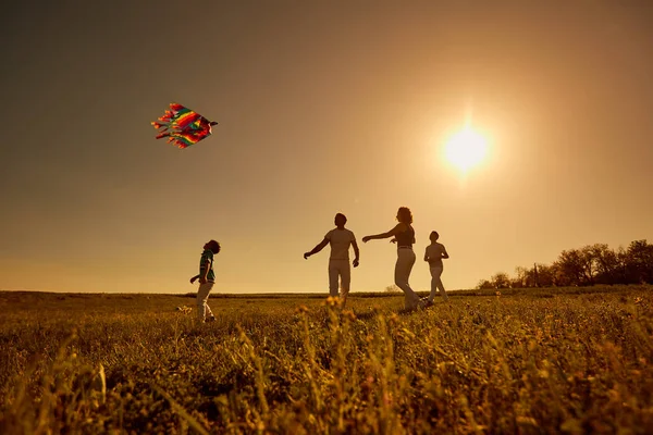Šťastná rodina s drakem hraje při západu slunce na poli — Stock fotografie