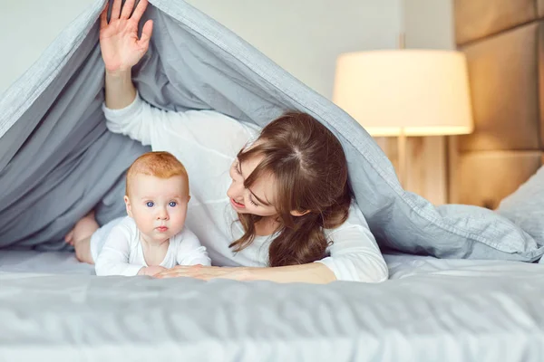 寝室のベッドの上に横たわる遊んで赤ちゃんと母. — ストック写真