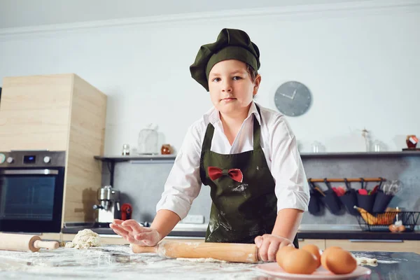 O menino está vestido como um cozinheiro na cozinha — Fotografia de Stock