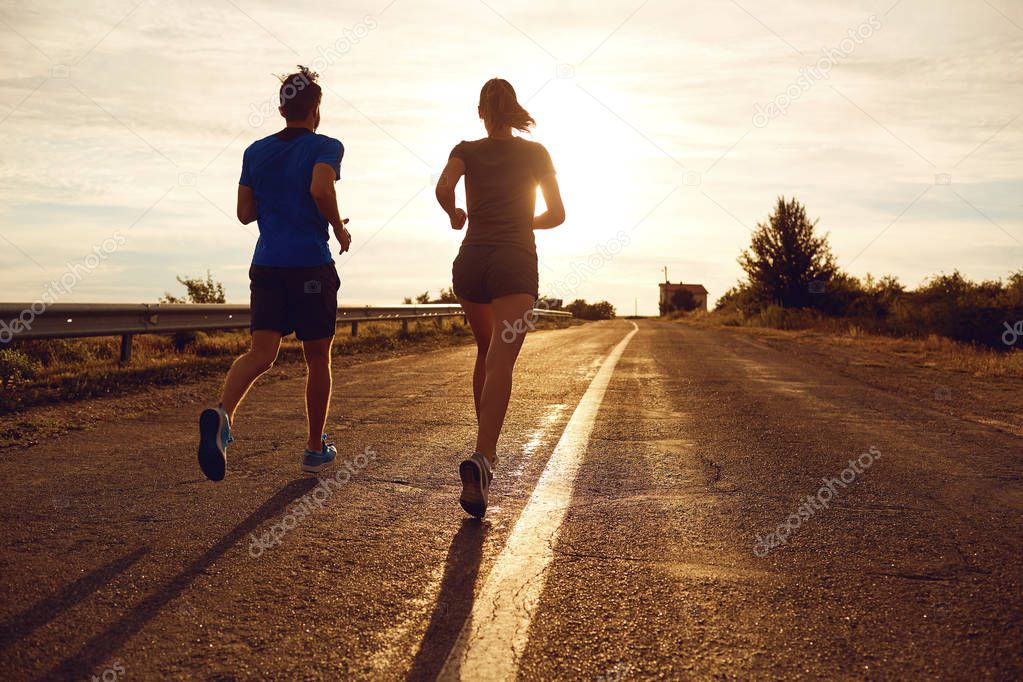 A guy and a girl jog along the road  in nature. 