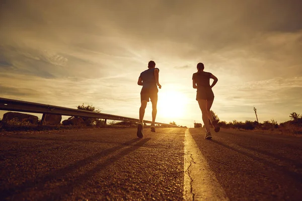 Ein Mann und ein Mädchen joggen in der Natur entlang der Straße. — Stockfoto