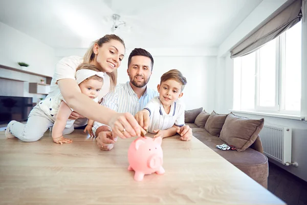 Eine lächelnde Familie spart Geld mit einem Sparschwein. — Stockfoto