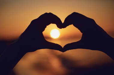 Deniz günbatımı üzerinde kalp şeklinde el.