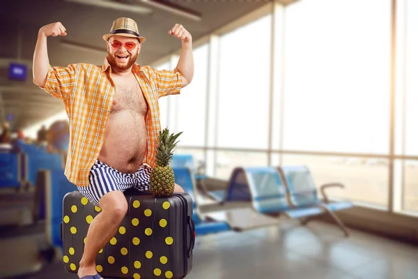 Ein lustiger dicker Tourist mit einem Koffer am Flughafen. — Stockfoto