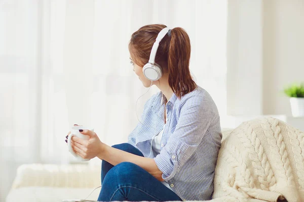 Una chica con auriculares escucha música mirando por la ventana  . — Foto de Stock