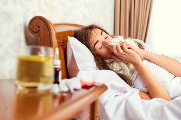 Una ragazza malata sdraiata su un letto che si pulisce il naso con una felpa . — Foto Stock