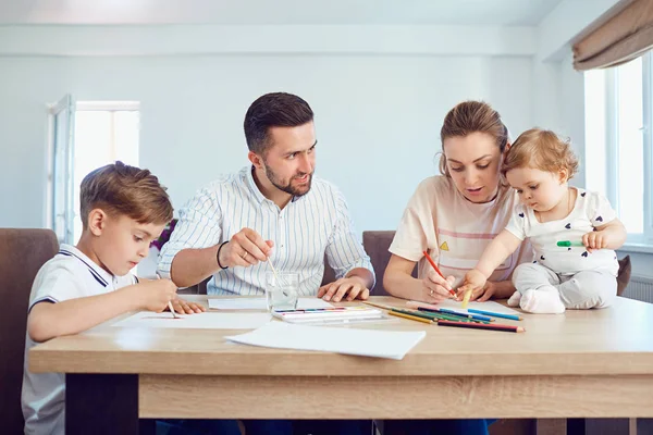 Família feliz desenha pinturas em um papel na mesa . — Fotografia de Stock