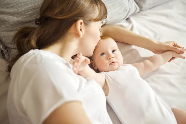 Feliz madre abrazando al bebé acostado en la cama en el interior . — Foto de Stock