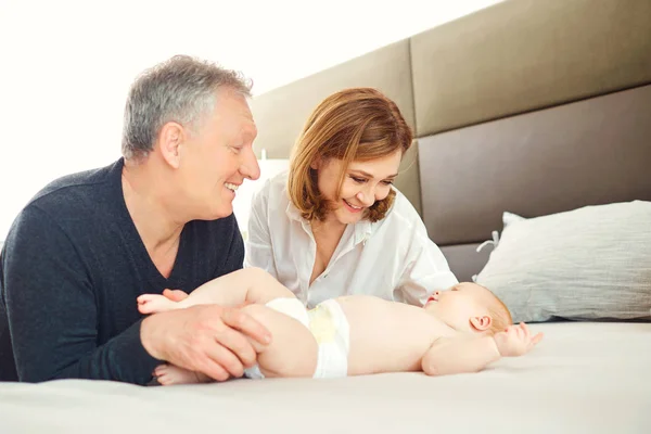 Abuelos y el bebé están jugando en la cama . — Foto de Stock