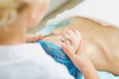 Şevval özçelik güzellik spa salonda genç bir kadın için yüz masajı yapar.