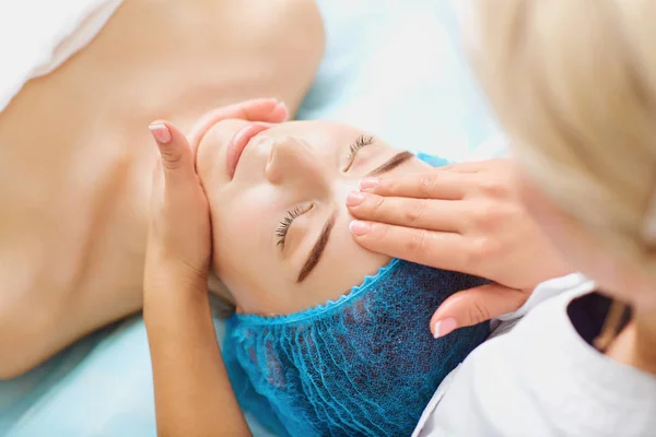 Schoonheidsspecialist maakt gezichtsmassage aan een jonge vrouw. — Stockfoto