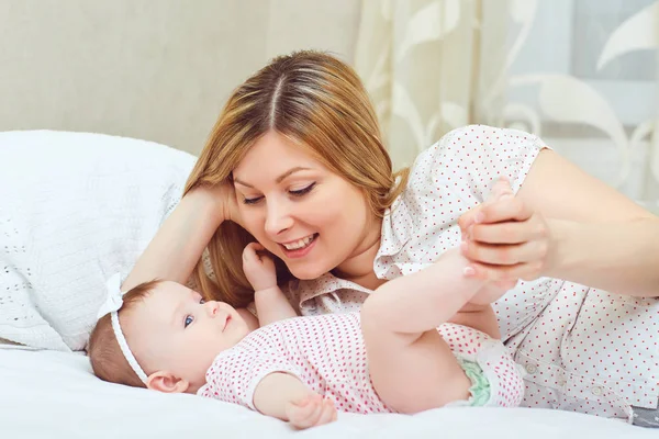 A happy mother with a baby plays on a bed. — Stock Photo, Image