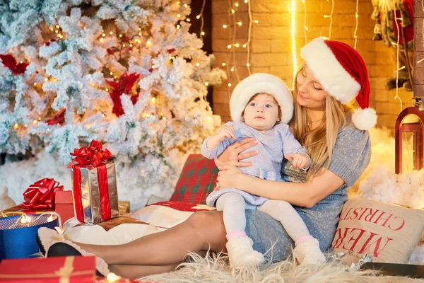 Moeder met baby in een hoed van de kerstman op de kerst-kamer. — Stockfoto
