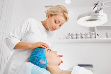 Kadın güzellik uzmanı bir kız yüzü inceliyor.