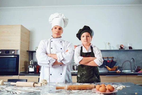 Cozinhe com o menino no uniforme do cozinheiro na cozinha . — Fotografia de Stock
