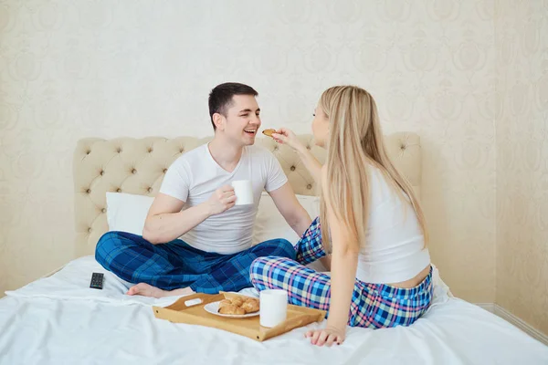 Um jovem casal está tomando café da manhã na cama . — Fotografia de Stock