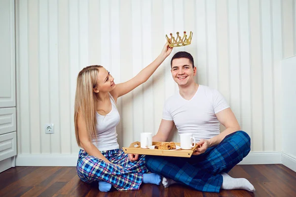 Um casal feliz em pijama sentar-se no chão em uma sala contra um — Fotografia de Stock