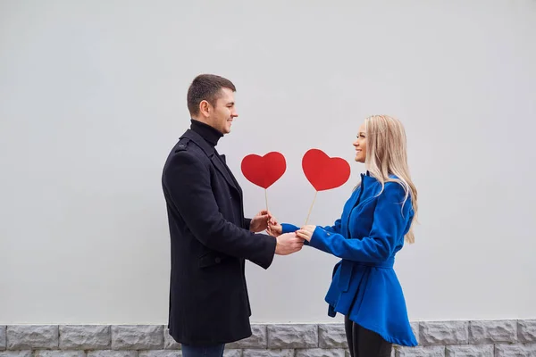 Um casal amoroso em um casaco com corações nas mãos . — Fotografia de Stock