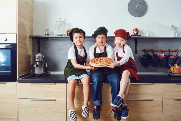 Um grupo de crianças em um terno de cozinha com pizza na cozinha — Fotografia de Stock