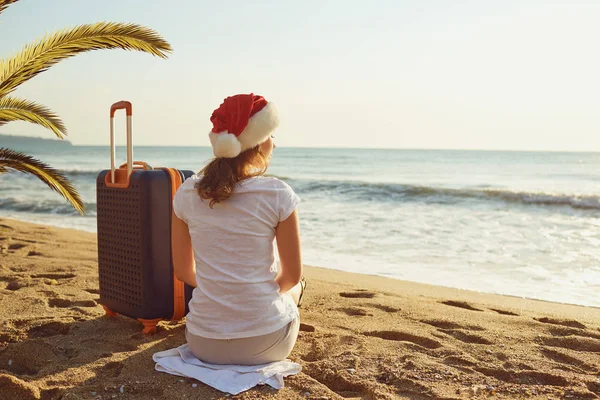 Дівчина в Санта-Клауса капелюх з валізою на березі моря на Різдв — стокове фото