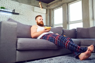 Kanepede oturan kalın sakallı adam yeme popcor.