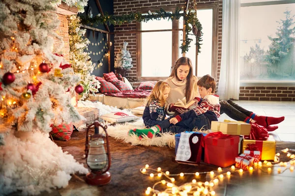 Mamá y los niños están leyendo un libro el día de Navidad . — Foto de Stock