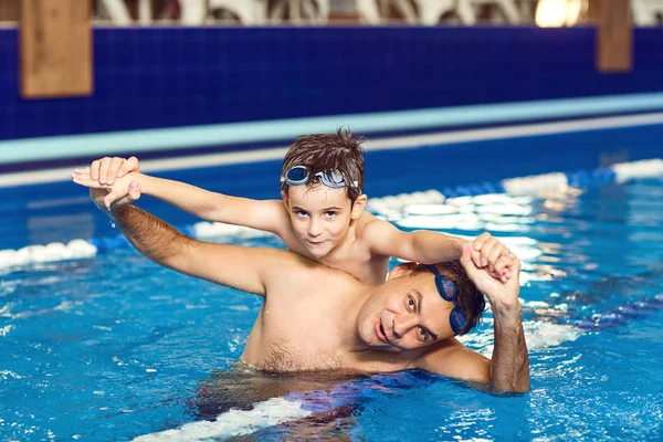 Father and son are playing in the water in a swimming pool.