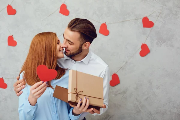A young couple gives a gift on a gray background. — Stock Photo, Image