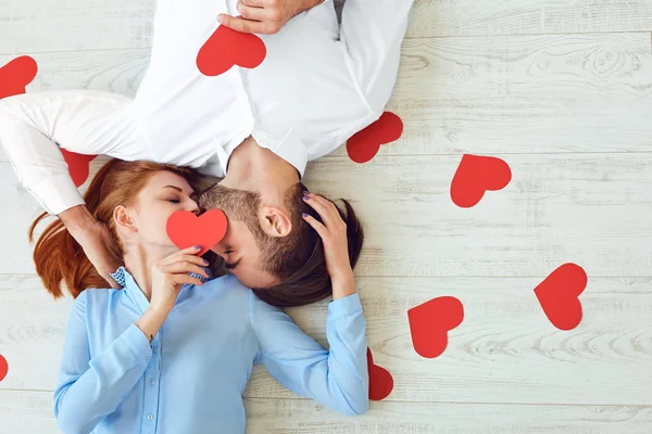 Casal beijos deitados em um soalho com um coração de papel — Fotografia de Stock