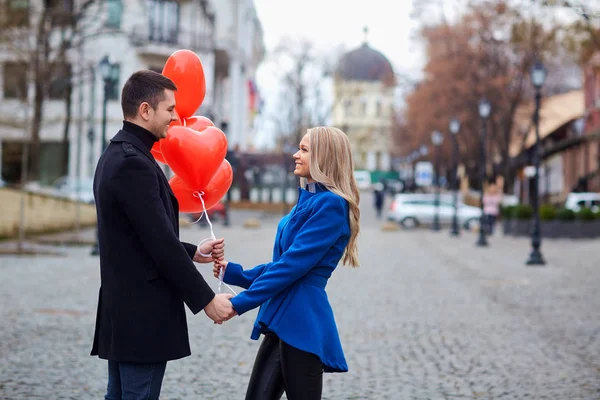 Una pareja amorosa en un abrigo con globos corazones en las manos . — Foto de Stock