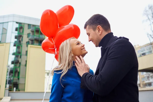 Una pareja cariñosa en un abrigo con globos corazones en las manos en una cit —  Fotos de Stock
