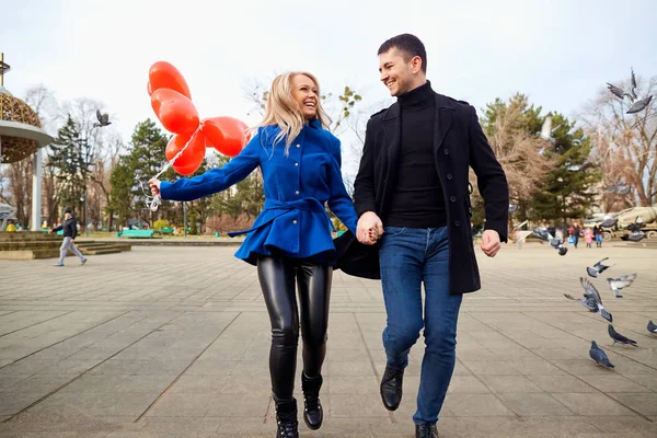 Um casal amoroso de casaco com balões de corações nas mãos — Fotografia de Stock
