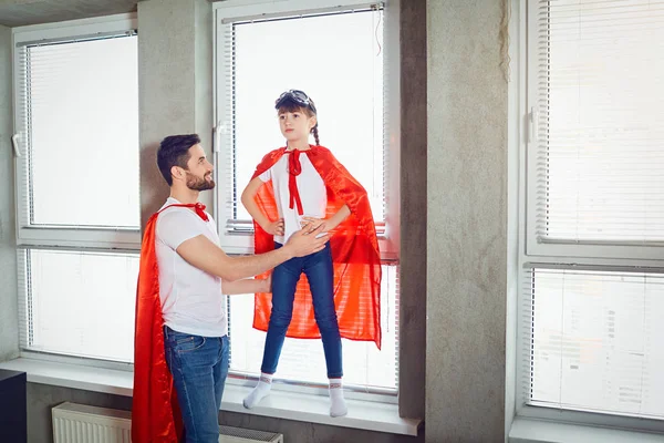 Батько і дочка дитина в костюмах супер герой грають в кімнаті . — стокове фото