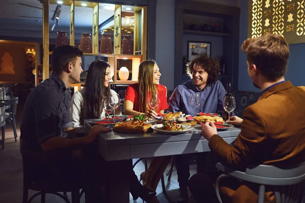 Um grupo de amigos ri em um restaurante ao jantar — Fotografia de Stock
