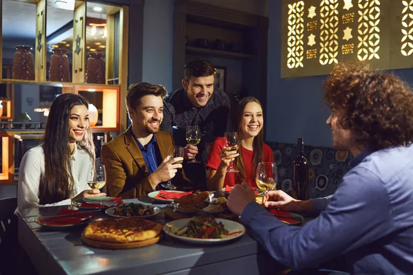 Amigos felices hablan en un restaurante por la noche . — Foto de Stock