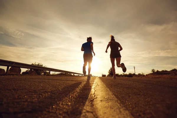 Mužem a ženou běhat po silnici při západu slunce v přírodě. — Stock fotografie