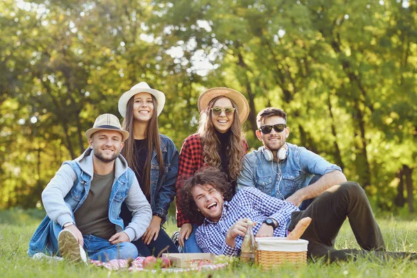 Young people laugh sitting on the grass at a picnic. — Stock Photo, Image