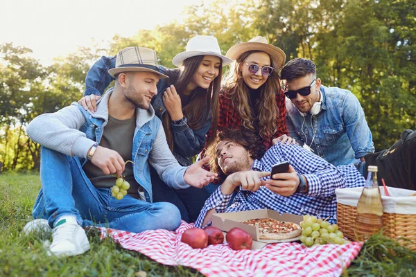 Young people laugh sitting on the grass at a picnic. — Stock Photo, Image