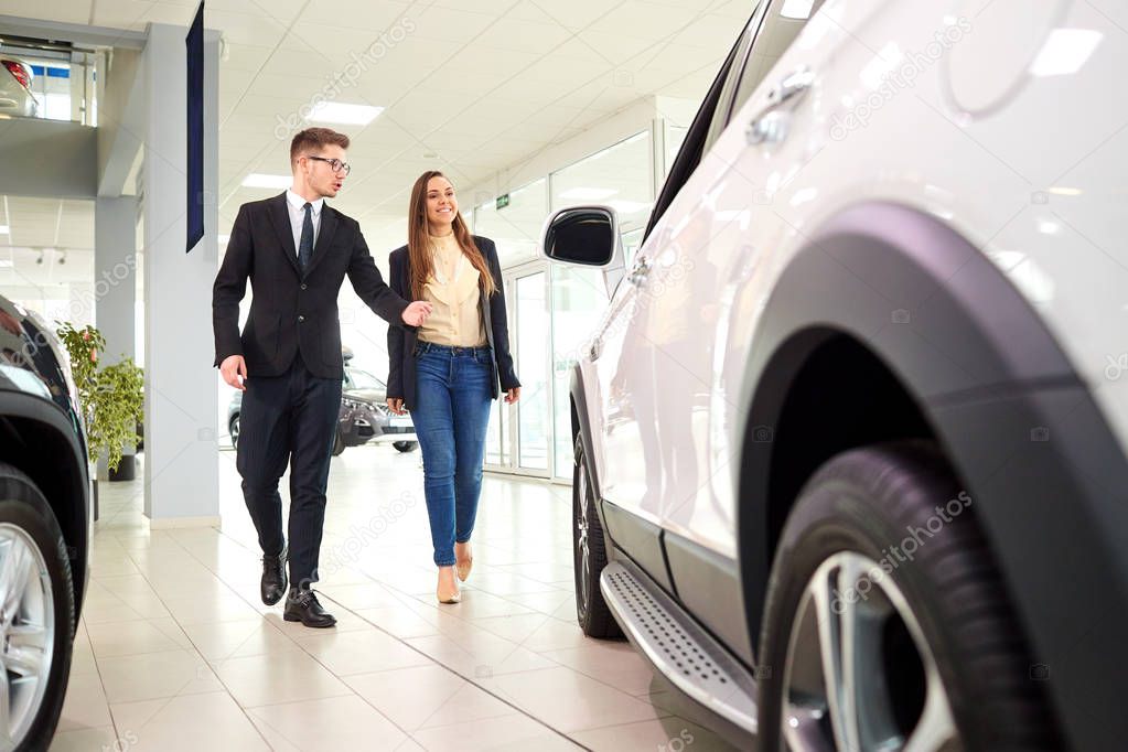 Girl and the salesman choose a car in the auto showroom