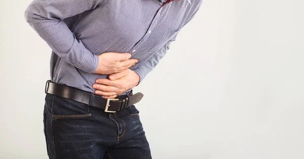 Un uomo soffre di dolori addominali. Dolore addominale. Il ragazzo con i vestiti apparenti che tiene la pancia con le mani . — Foto Stock