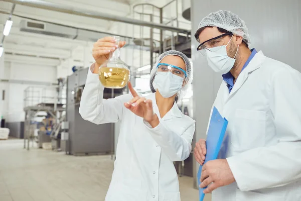 Trabalhadores em máscaras e casacos olham para o líquido no frasco no trabalho — Fotografia de Stock