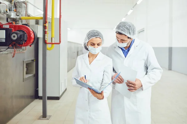 Twee technologen in lab jassen en maskers in de fabriek. — Stockfoto