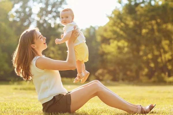 Mutter mit Kind spielt bei Sonnenuntergang im Gras. — Stockfoto