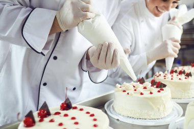 Two pastry chefs decorate a cake from a bag in a pastry shop clipart