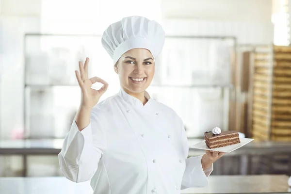 La pastelera sostiene un pastel en su mano en la panadería. . — Foto de Stock